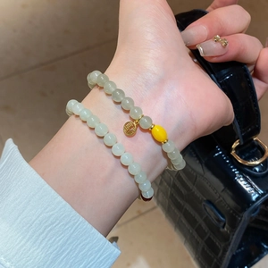Détail de perles de jade vert clair et bracelet à breloque Fu dorée au poignet