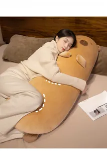 Close-up of a long Capybara plush pillow being held on a bed, showing soft texture