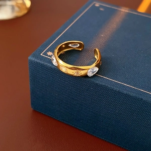 Detail of gold-tone ring with clear zircons and star engraving on dark velvet box