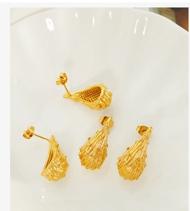 Macro detail of gold-plated teardrop earrings with unique textured hollow design on a white tray
