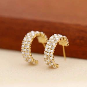 Close-up of C-shaped gold earrings with rows of white pearls and sparkling zircons