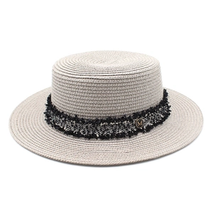 Detail of beige straw boater hat with black fringed ribbon and gold M emblem