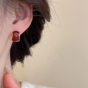 Close-up of elegant burgundy rectangular earring with gold border on a female model