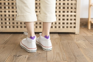 Detail of purple low cut socks with heart heel design paired with white canvas sneakers