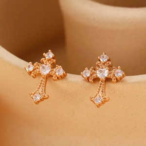 Detail view of gold cross ear stud with white zircons on a beige ceramic holder