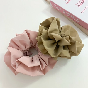 Detail shot of large satin flower bud scrunchies in pink and khaki on a white surface