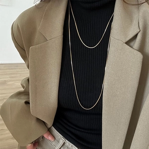 Detail of layered gold snake bone chains worn over a chic beige blazer outfit