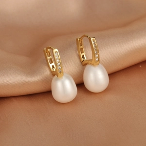 Macro shot of 18K gold plated pearl earrings with zircon inlay on silk background