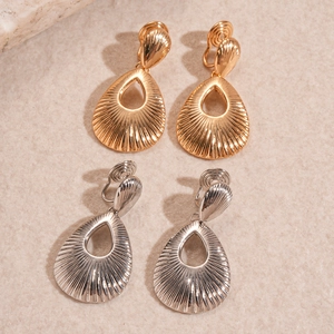 Detail of gold and silver teardrop ear clips with radial stripes on textured stone