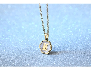 Macro shot of hexagonal gold titanium pendant with white pearl inlay and letter M