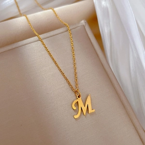 Macro view of gold M-shaped pendant necklace on beige jewelry display tray