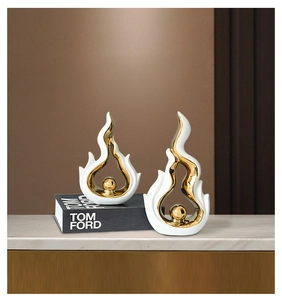Close-up of white and gold ceramic flame sculptures on marble surface with luxury book