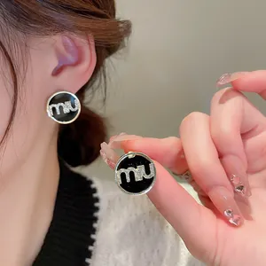 Macro shot of gold-plated round earrings featuring black enamel and crystal letter mu
