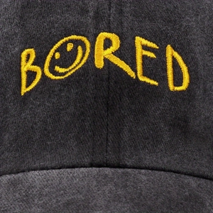 Detailed close-up of yellow BORED embroidery with smiley face on charcoal grey baseball cap