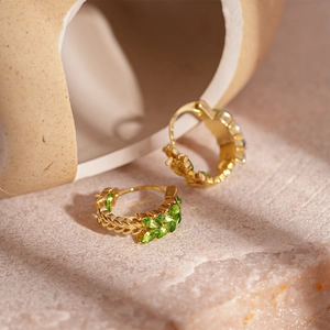 Detail of gold wheat ear hoops with marquise green gems on natural stone