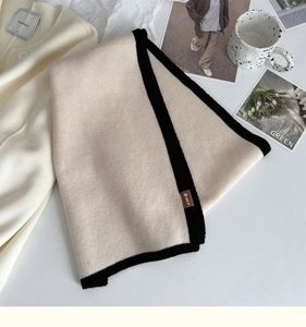 Detailed close-up of a knit scarf with black contrast edging and a brown leather logo tag