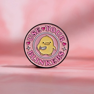 Detail of cartoon yellow duck holding knife enamel pin with USE YOUR BLINKERS text