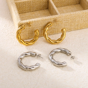Detailed view of gold and silver twisted C-shaped earrings on a textured background