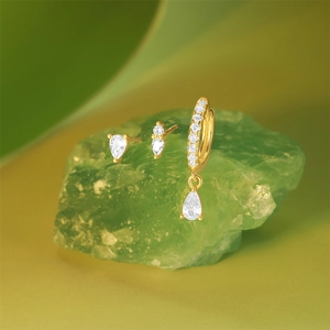 Macro shot of 925 silver gold-plated earring set with teardrop zircons on a green stone