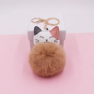 Detail of cute tricolor cat plush keychain with soft brown pompom and gold metal ring