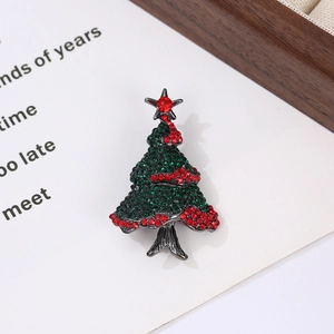 Detailed close-up of a Christmas tree brooch with green and red rhinestones on card
