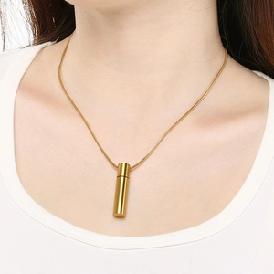 Close-up of golden cylindrical pendant with snake chain on a female model