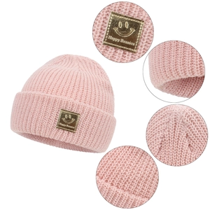 Detail view of pink knit beanie showing the golden smiley face patch and ribbed texture
