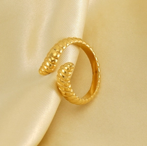 Macro detail of golden ribbed croissant open ring on champagne satin fabric background