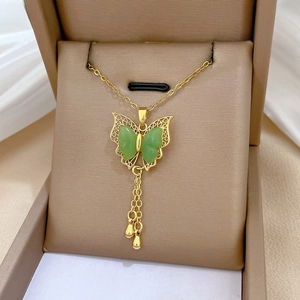 Detail view of a gold butterfly pendant necklace with green wings and elegant tassels