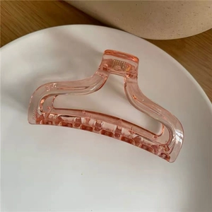 Top view of a translucent peach pink acrylic hair claw clip on a white round tray