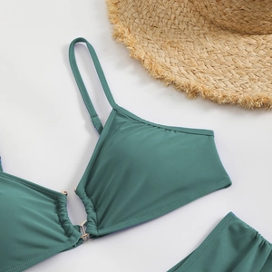 Detailed view of teal bikini top with center ring detail, ruching and straw hat on background