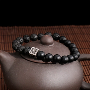 Detail of beaded bracelet with black lava rock and vintage silver letter M block