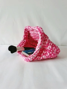 Detailed top view of handmade pink woven crochet cloud bag with makeup essentials inside