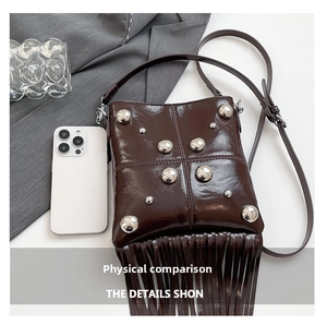Detail of dark brown vintage envelope bag with silver studs and long fringe next to a phone