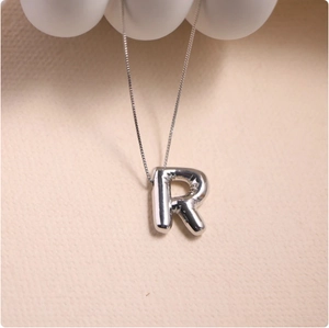 Macro view of silver balloon-style letter R pendant with metallic fold textures