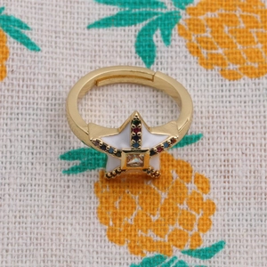 Macro shot of gold star ring with colorful stones and white enamel on pineapple fabric