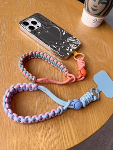Detail of adjustable woven phone lanyards with a metallic heart-shaped case on wood