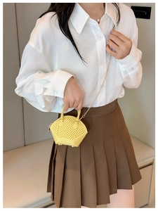 Detailed view of mini yellow shell bag with woven texture and gold chain worn by a model