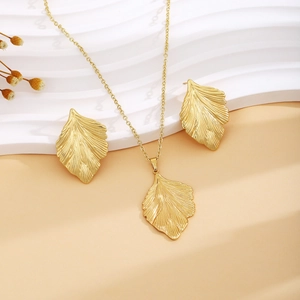 Elegant gold leaf shape necklace and earrings set on a minimalist textured background