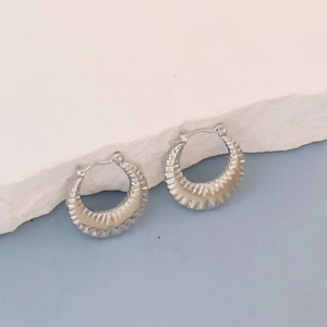 Detail of silver oval earrings with radiant pleated texture on a textured stone surface