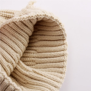Close-up of beige chunky knit texture and soft yarn weave on a winter beanie hat