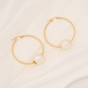 Macro view of gold minimalist hoop earrings with large white pearls on white silk fabric
