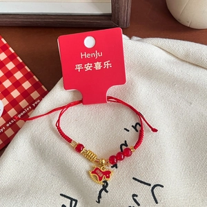 Macro view of woven red string bracelet with gold charms and round red glass beads