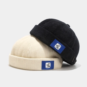 Corduroy docker hats in black and cream with blue label patches on a grey background