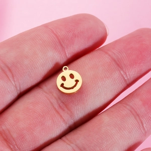 Macro shot of a 9mm gold stainless steel smiley face charm held on a finger