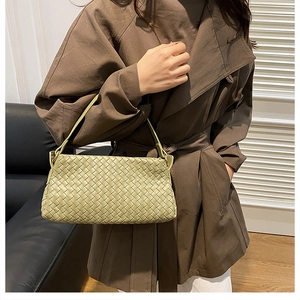 Dettaglio della borsa in pelle intrecciata verde chiaro portata da una modella in trench