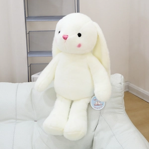 Close-up of a white plush rabbit toy with pink embroidery details sitting on a sofa