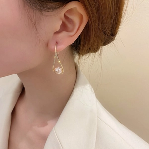 Fashionable gold teardrop earrings with crystals and white pearl on a female model
