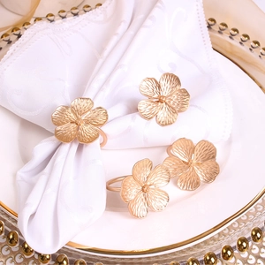 Close-up of matte gold flower napkin rings on white cloth and elegant table setting