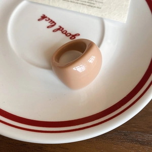 Close-up of minimalist beige resin oval ring on a white ceramic plate with red text
